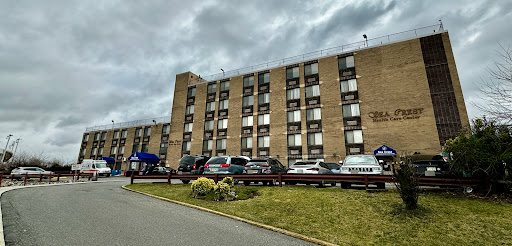 A view of a hotel building with vehicles parked in front under a cloudy sky.
