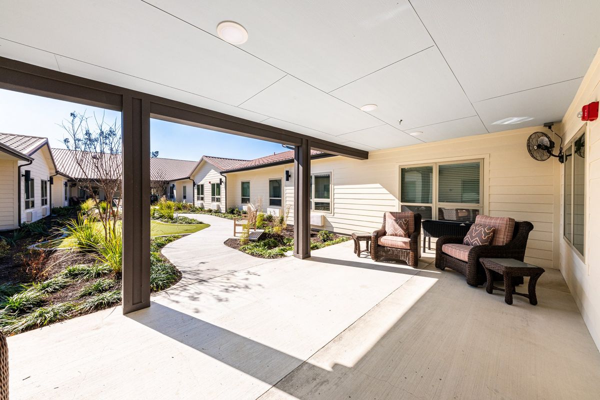 A sunny outdoor patio with comfortable seating and a view of a garden.