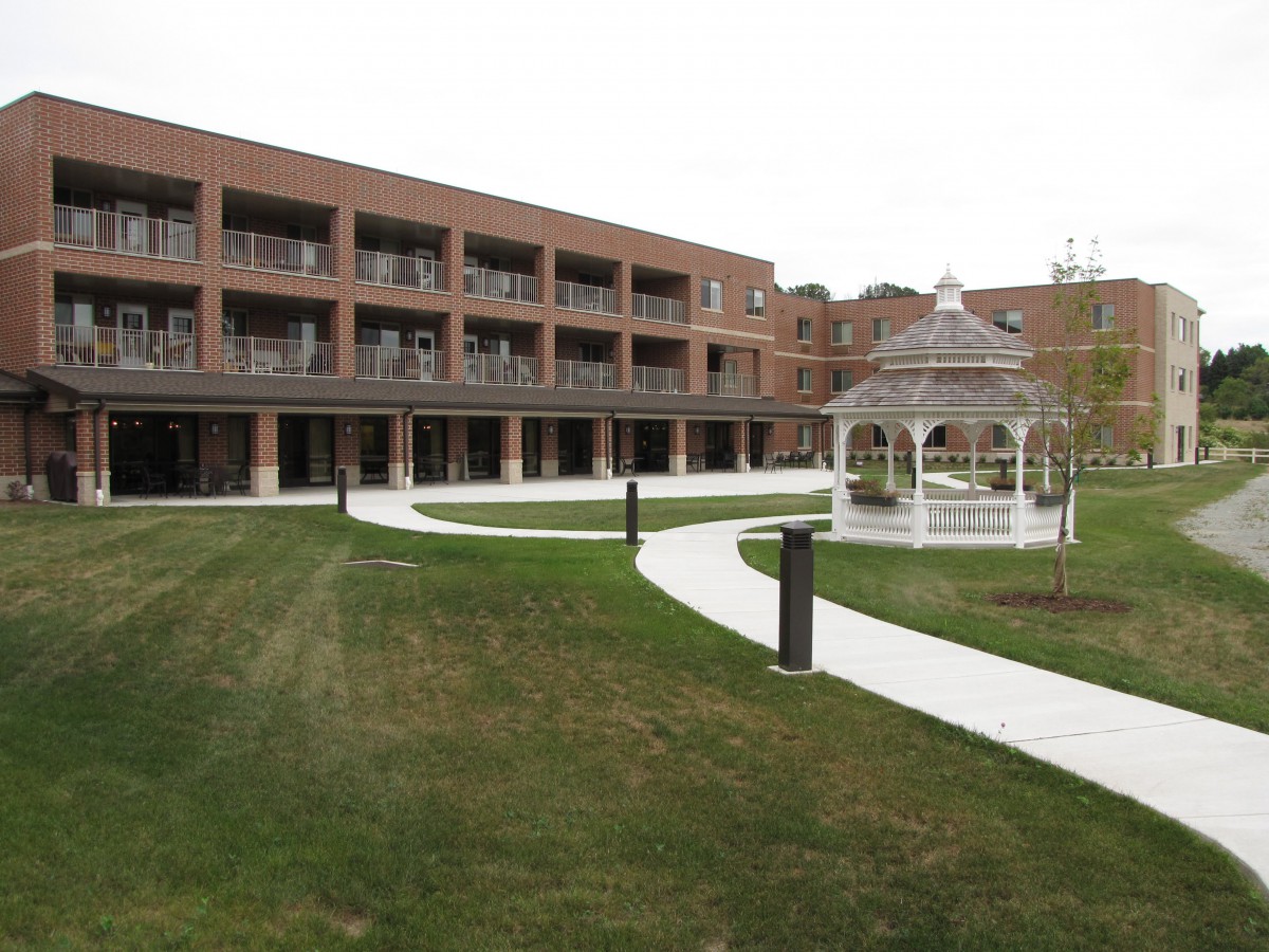 A brick building with balconies overlooks a well-maintained lawn featuring a gazebo and winding pathways.