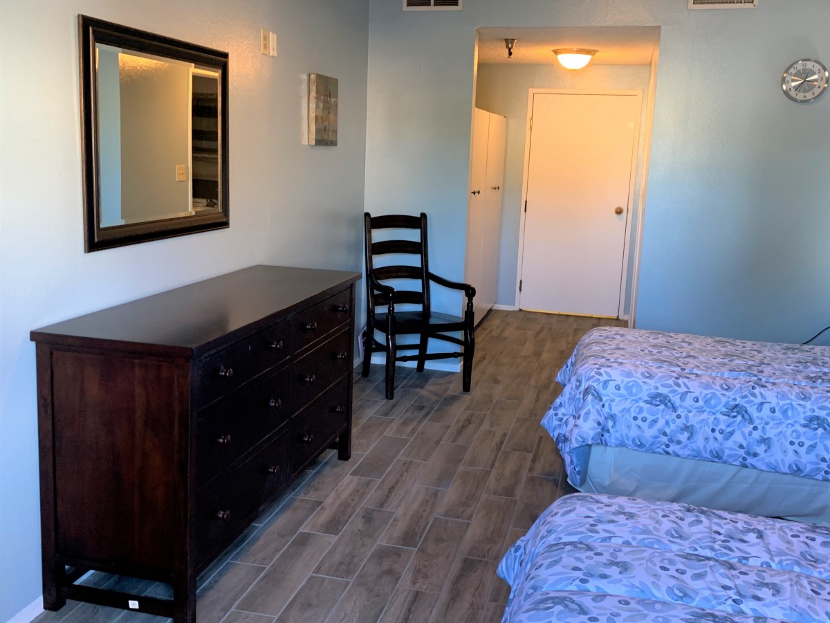 A neatly arranged bedroom featuring twin beds, a dresser with a mirror, and a wooden chair on a wooden floor.