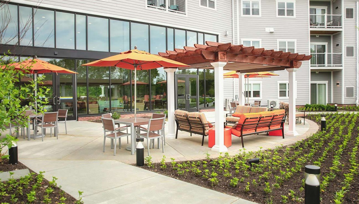 A modern outdoor patio area with seating, pergolas, and umbrellas at a residential or commercial building.