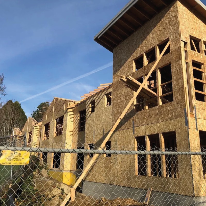 A partially constructed building with a wooden framework and scaffolding, surrounded by a fence on a clear day.