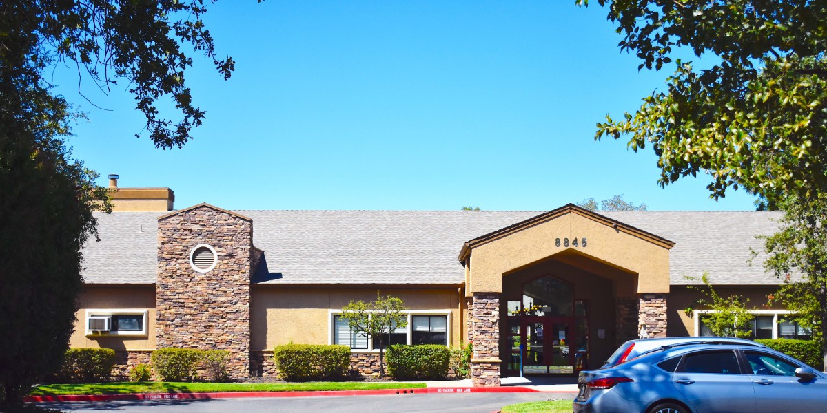 A community center building with a stone facade and peaked roof, surrounded by trees and under a clear blue sky.
