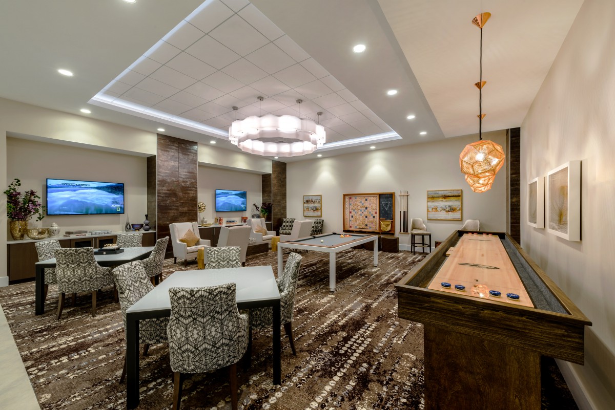 A modern game room with shuffleboard, stylish chandeliers, and comfortable seating.