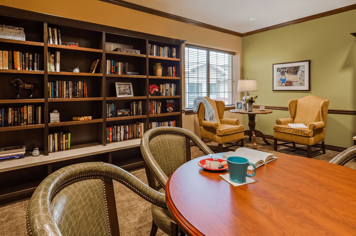 A cozy reading room with a large bookshelf, comfortable chairs, and a table with a mug.