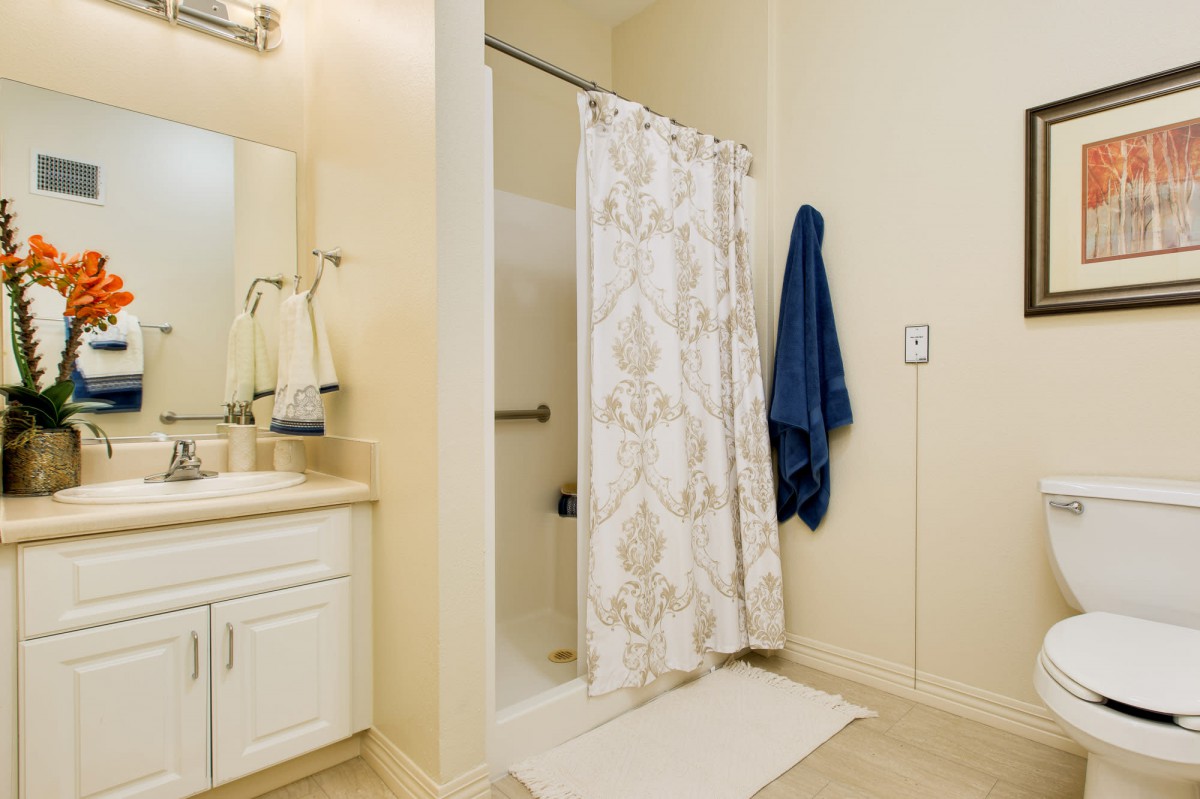 A bathroom featuring a shower with a floral curtain, a nearby sink with a mirror, and a blue towel hanging on the wall.