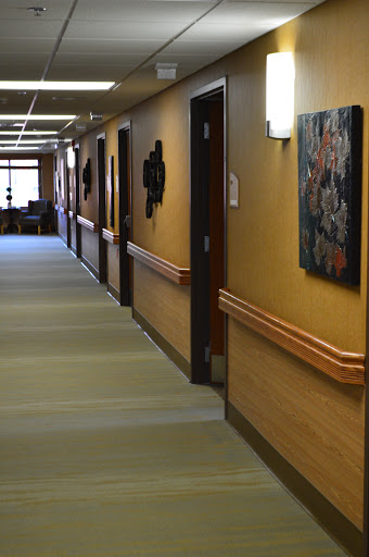 A serene hospital hallway adorned with artwork, featuring doors to patient rooms.