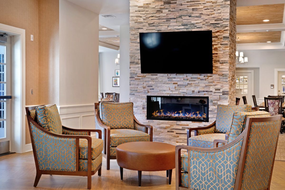 A cozy living room with a stone fireplace, comfortable chairs, and a television mounted above.