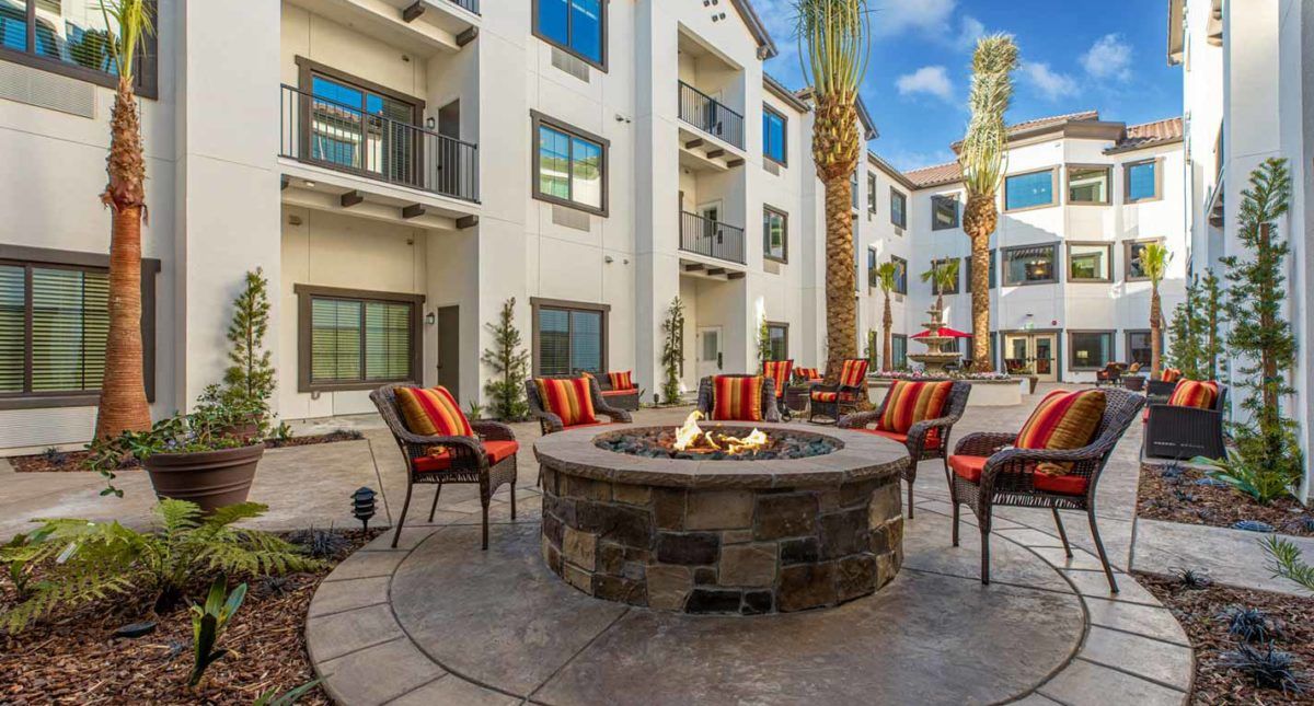A modern apartment complex patio area featuring a central fire pit surrounded by colorful outdoor seating.