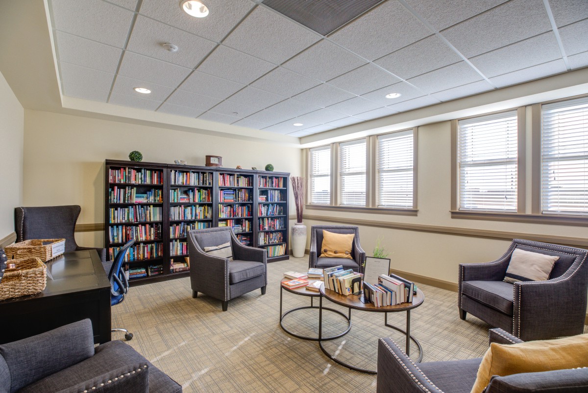 A cozy library corner with armchairs and bookshelves, well-lit by ample natural light from large windows.