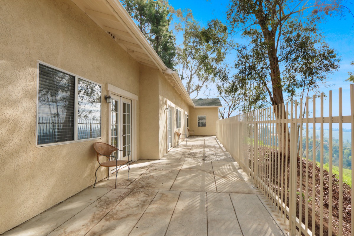 A spacious outdoor patio with a view, featuring a fenced area and surrounded by tall trees.