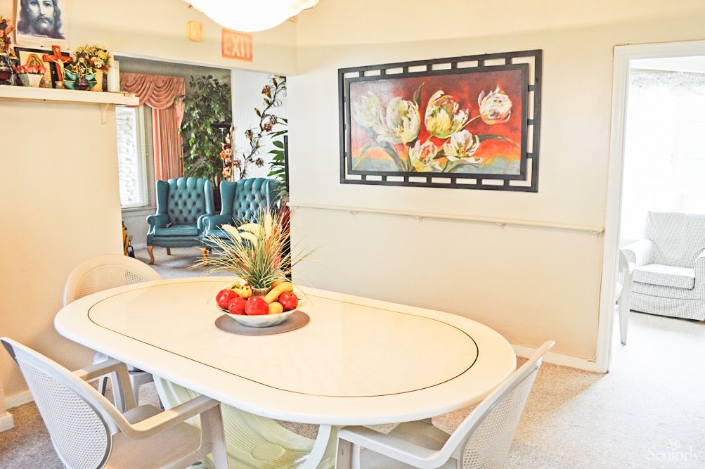 A bright and stylish dining room featuring a white table set, colorful fruit bowl centerpiece, and vibrant wall art.