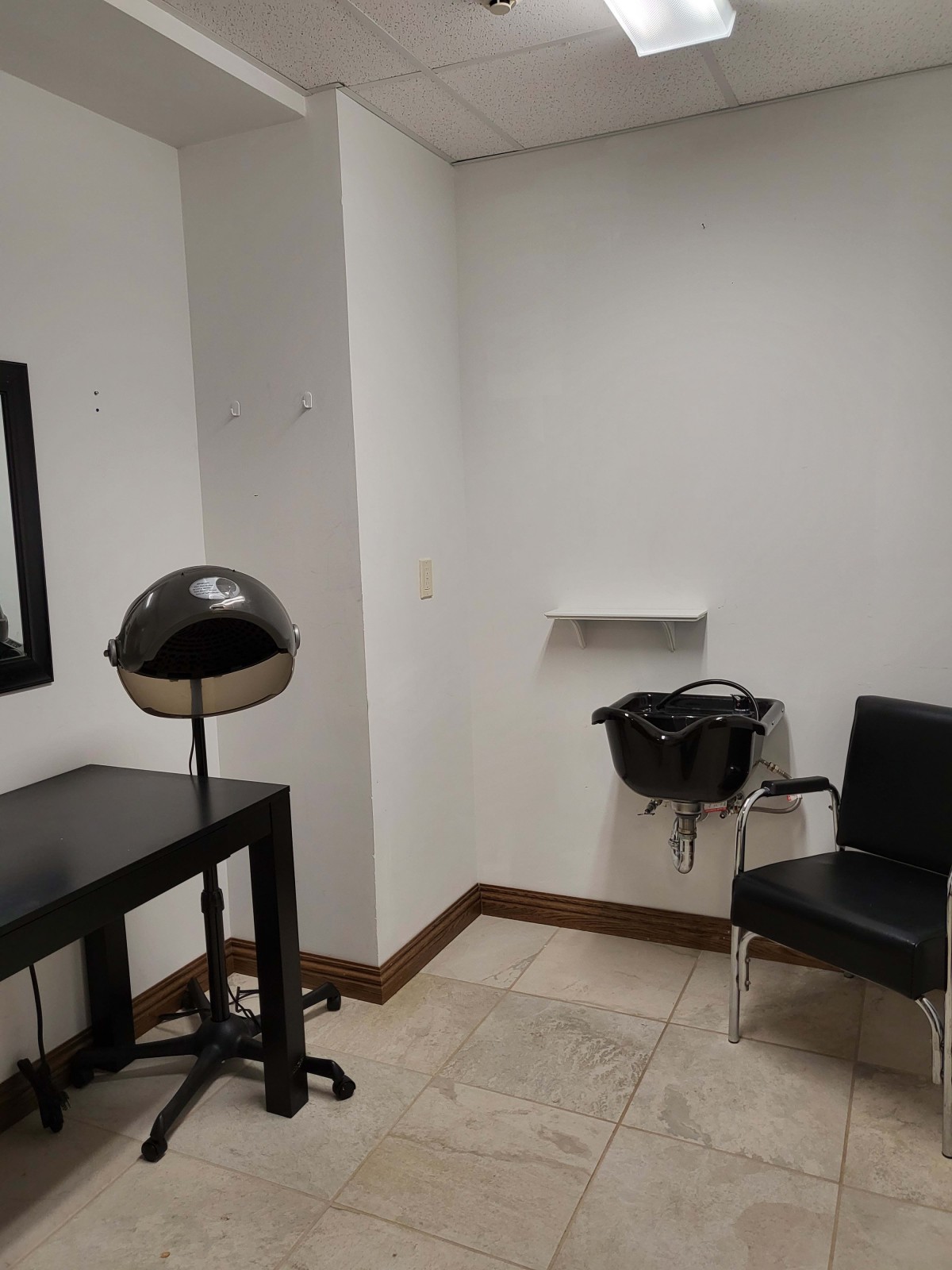 A small salon room with a hairdryer, chair, and mirror.