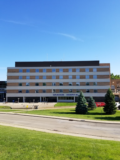 A modern university building set against a clear blue sky, surrounded by well-maintained grass and trees.