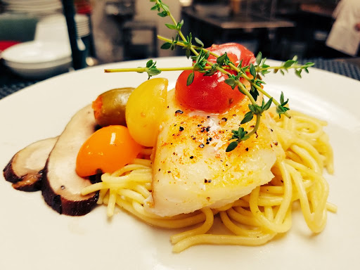 A beautifully plated dish featuring fish on a bed of pasta, garnished with fresh herbs and colorful cherry tomatoes.