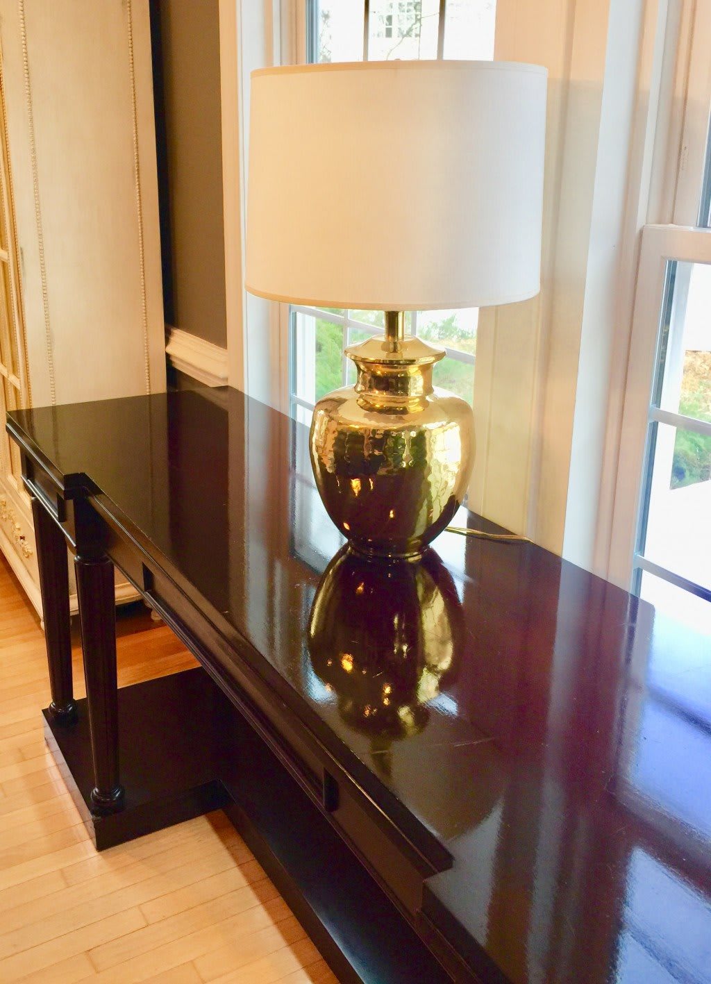A stylish gold lamp on a glossy wooden table next to a window.