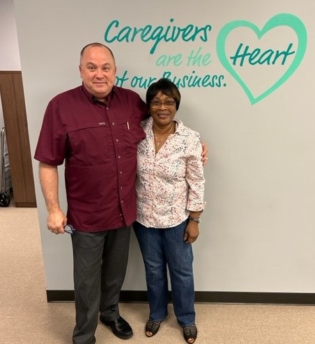 Two people standing together in front of a wall with a message about caregivers and heart.