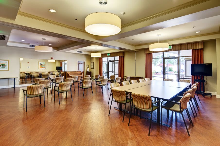 A spacious dining area with multiple tables and chairs, featuring a wooden floor and large ceiling lights.