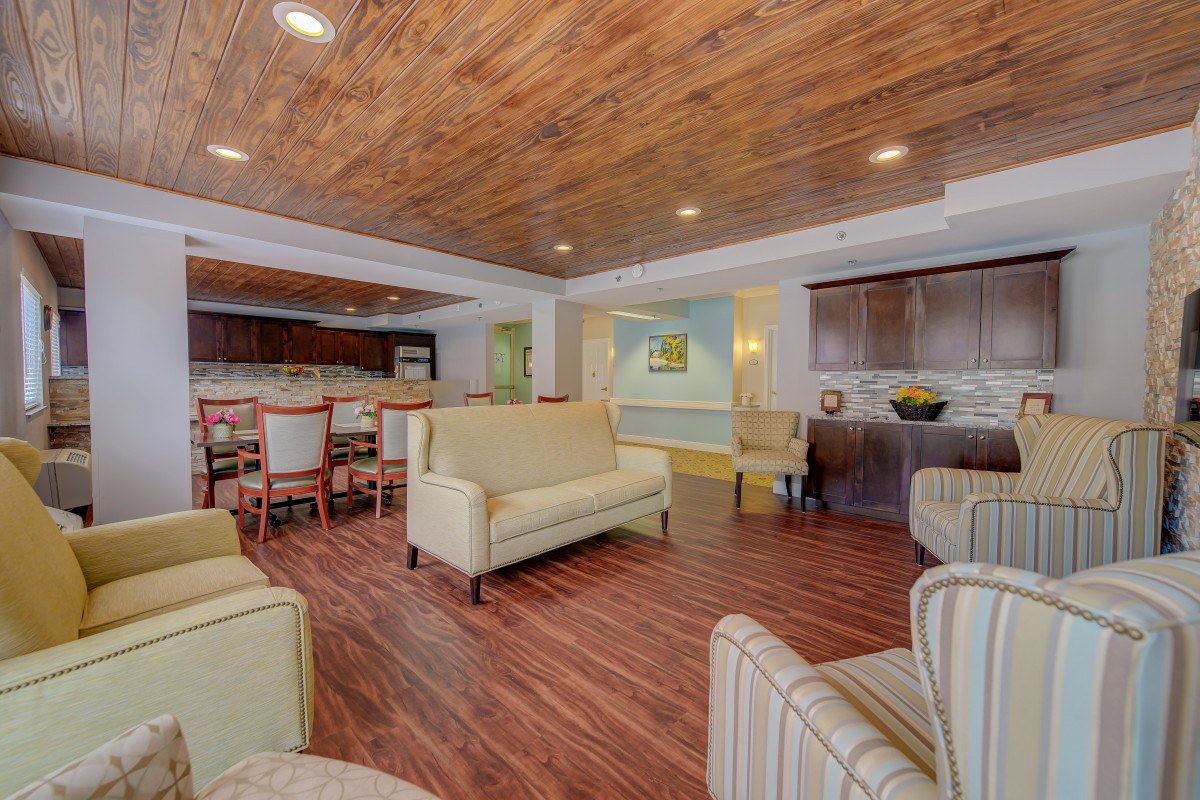 A cozy lounge with wooden ceilings and comfortable seating, including armchairs and a sofa, next to a dining area.