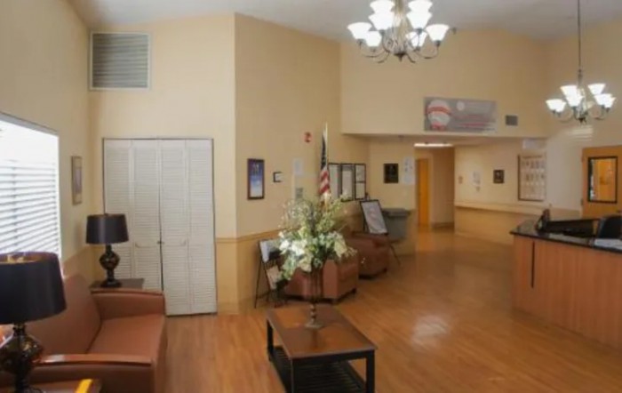 A spacious lobby with comfortable seating, an American flag, and decorative flowers under a chandelier.