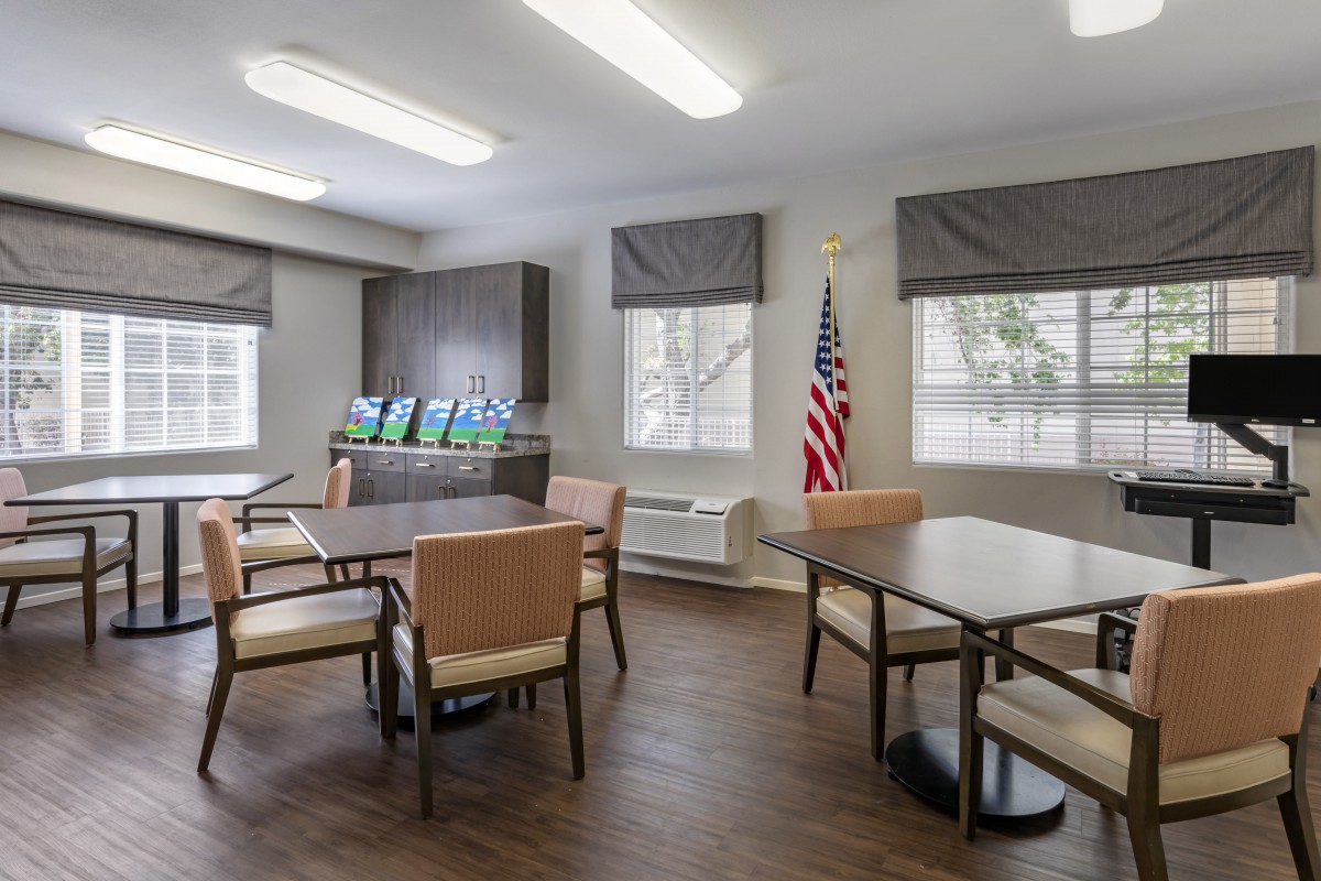 A well-lit room with tables and chairs, featuring a flag and large windows.