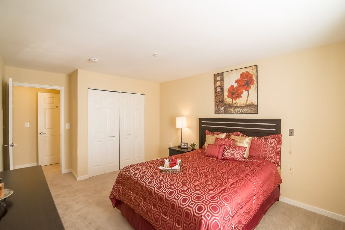 A cozy bedroom with red bedding, artwork on the wall, and a nightstand with a lamp.