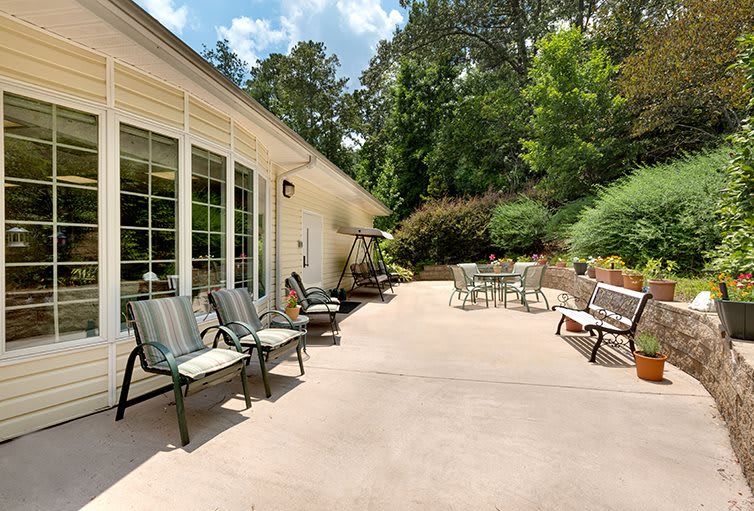 A spacious backyard patio with various seating options, surrounded by lush greenery on a sunny day.