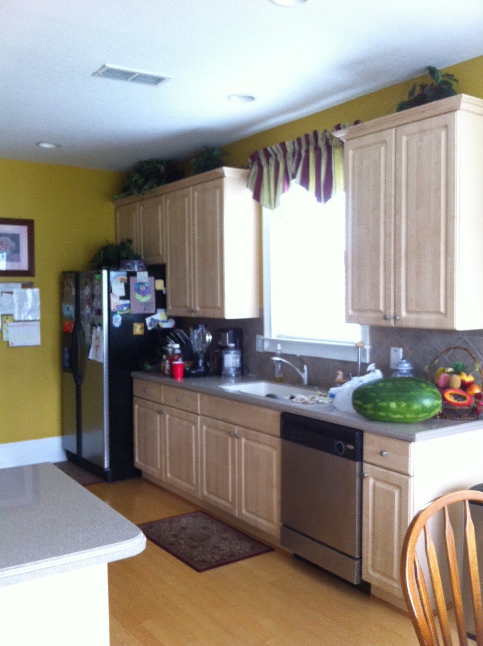 A modern kitchen with wooden cabinets, a refrigerator, and a countertop featuring a watermelon and fruit basket.