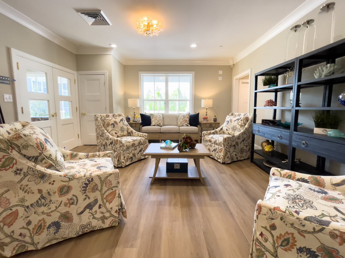 A cozy living room with patterned chairs and a comfortable sofa arranged around a central coffee table, complemented by wood flooring and ample natural light.