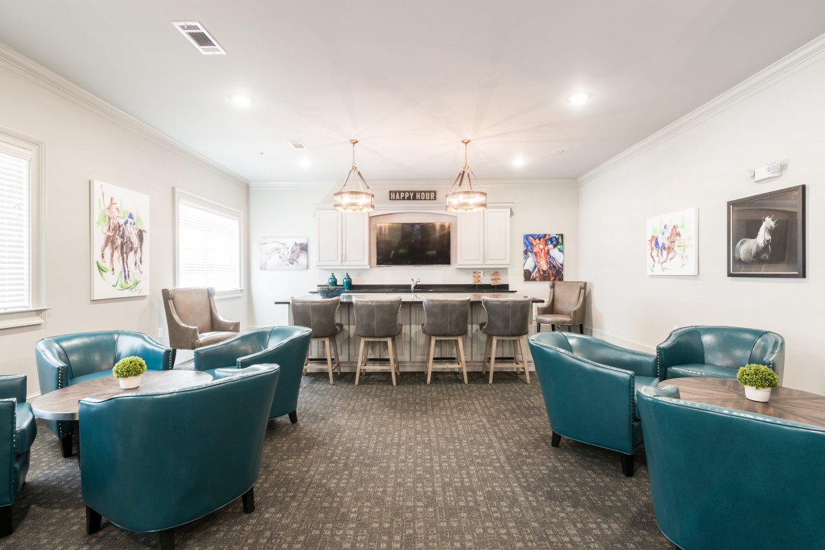 A modern lounge area featuring armchairs, bar stools, and a large television.