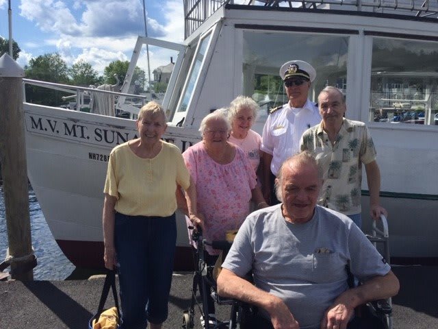 A group of people posing in front of a boat on a sunny day.