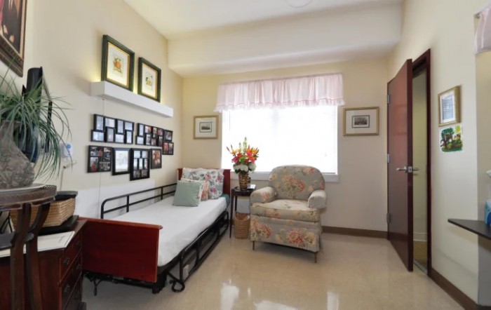 A cozy bedroom with a daybed and armchair, adorned with photo frames and floral decor.