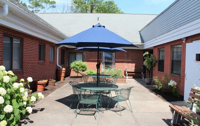 A sunny courtyard with a blue umbrella over outdoor furniture, surrounded by brick buildings.