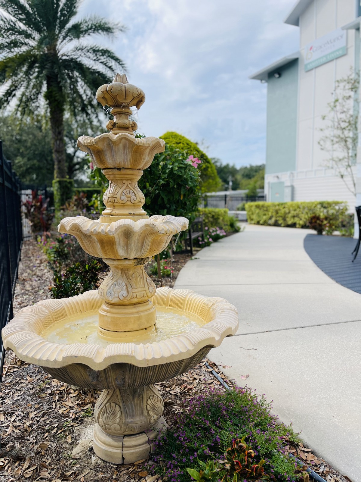 A decorative three-tiered fountain in a garden setting with a curving pathway.