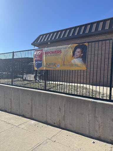 A promotional banner displayed on a fence in front of a building under clear blue skies.