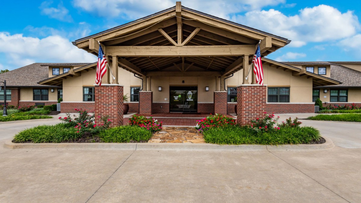 A brick building entrance adorned with American flags and surrounded by neat landscaping.