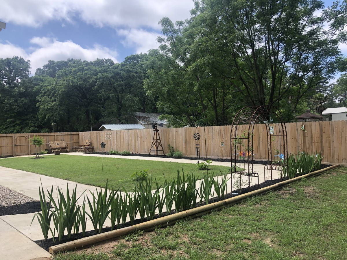A neatly landscaped garden with a central lawn, bordered by a wooden fence and surrounded by trees.