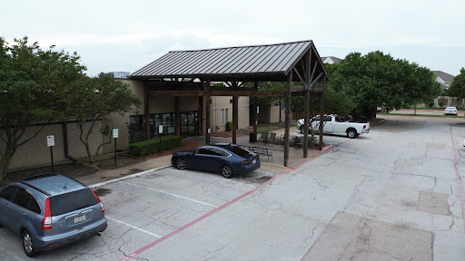 A modern building with a metal roof and a covered entryway, surrounded by a parking lot.