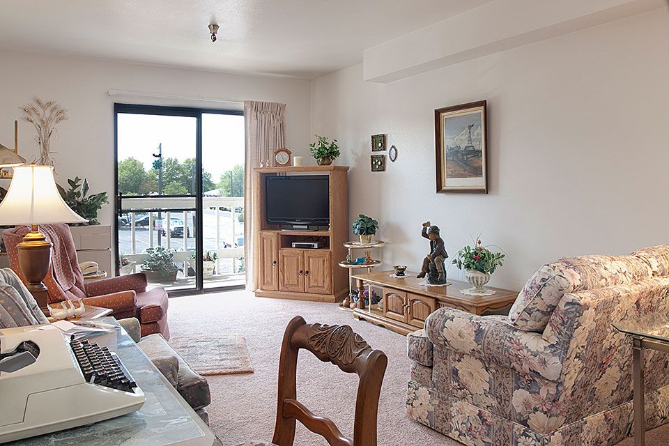 A cozy living room with vintage decor, featuring a floral sofa, television, and natural lighting.