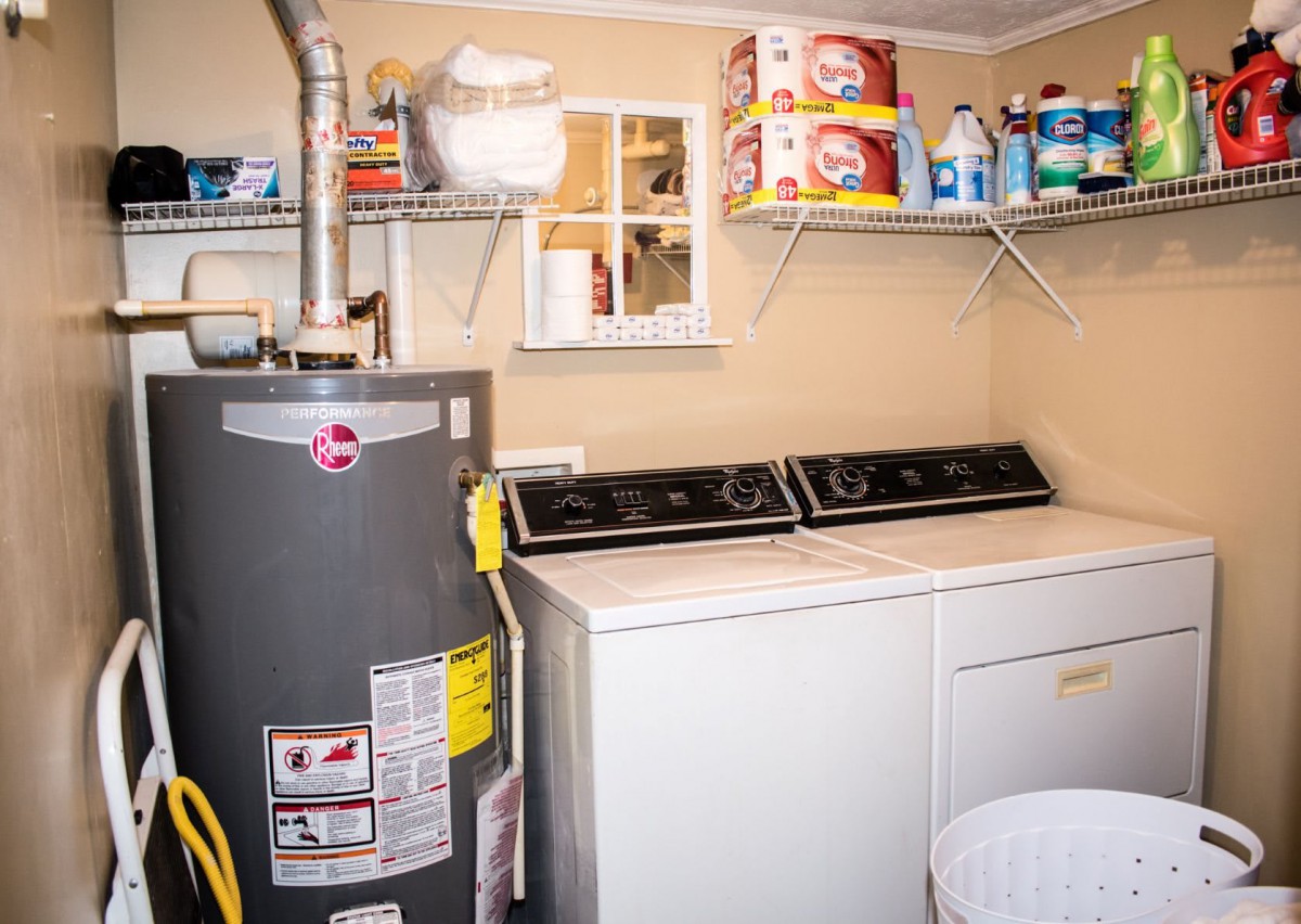 A utility room featuring a water heater, washer and dryer, with shelves stocked with detergents and other cleaning supplies.