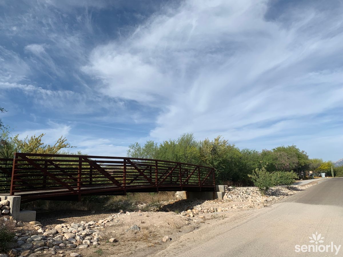 A metal bridge extends across a dry, rocky area under a vast blue sky with scattered clouds.