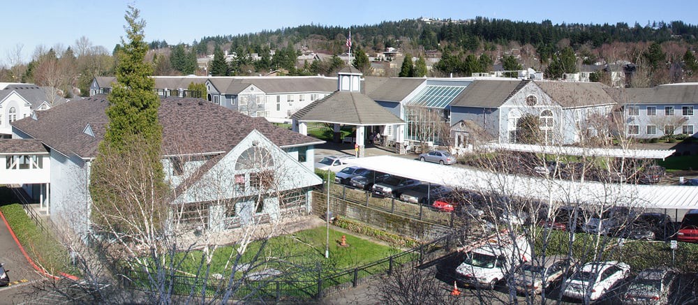 An aerial view of a residential area with several buildings, cars parked, and trees in the background.