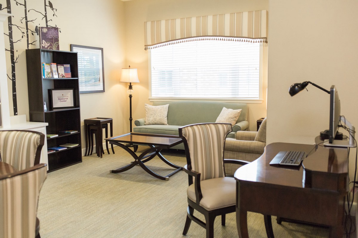 A cozy and well-lit living room with modern furniture, including a sofa, chair, desk, lamp, and bookcase.