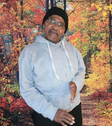 A person wearing a hoodie stands against a vibrant autumn backdrop.