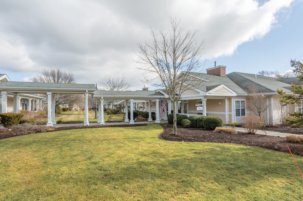 A residential house with a large lawn and covered porch under a cloudy sky.