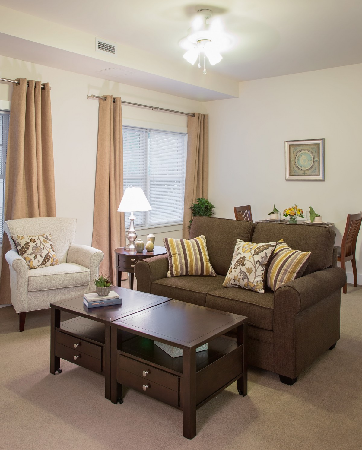 A cozy living room with a brown sofa, an armchair, and a wooden coffee table adorned with decorative pillows and modern decor.