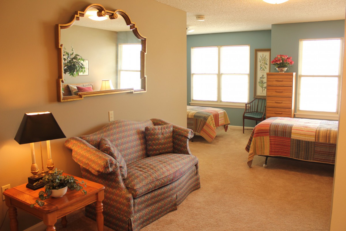 A cozy bedroom with twin beds, a sofa, and a large mirror reflecting natural light from the window.