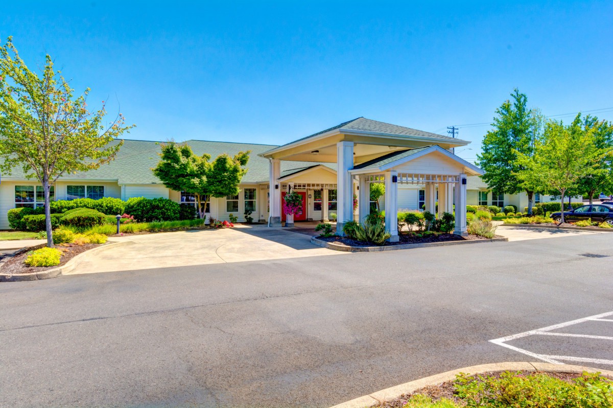 A building entrance with a covered driveway and landscaped surroundings under a clear blue sky.