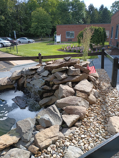 A serene waterfall feature surrounded by rocks and pebbles, with greenery in the background.