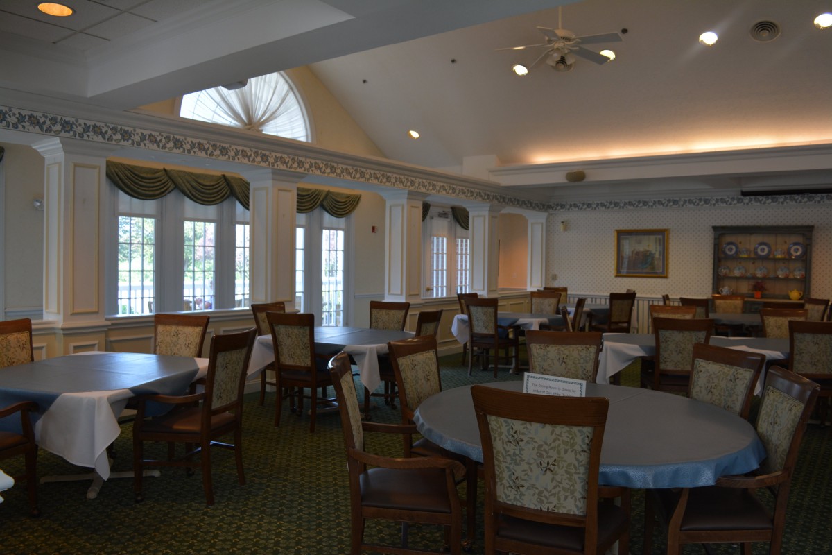 An empty dining room with multiple tables and chairs, featuring large windows.